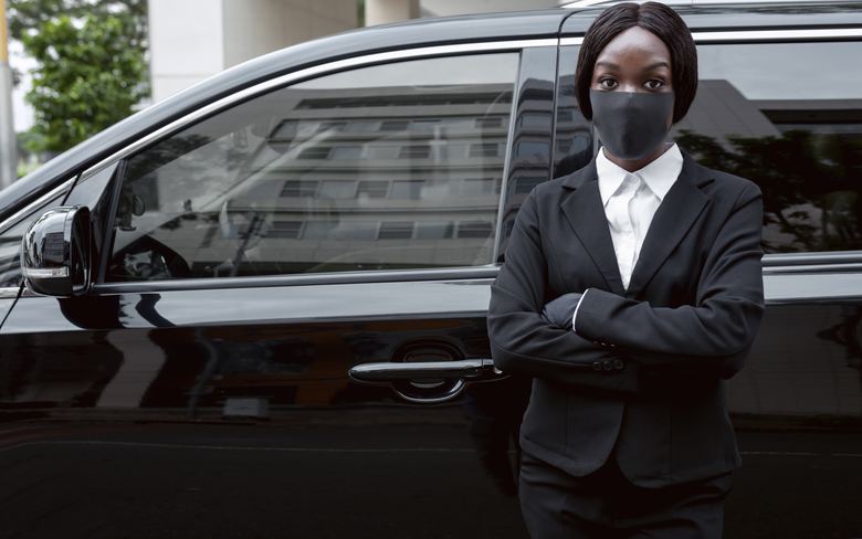 Chauffeur en costume sombre devant un corbillard à Cotonou